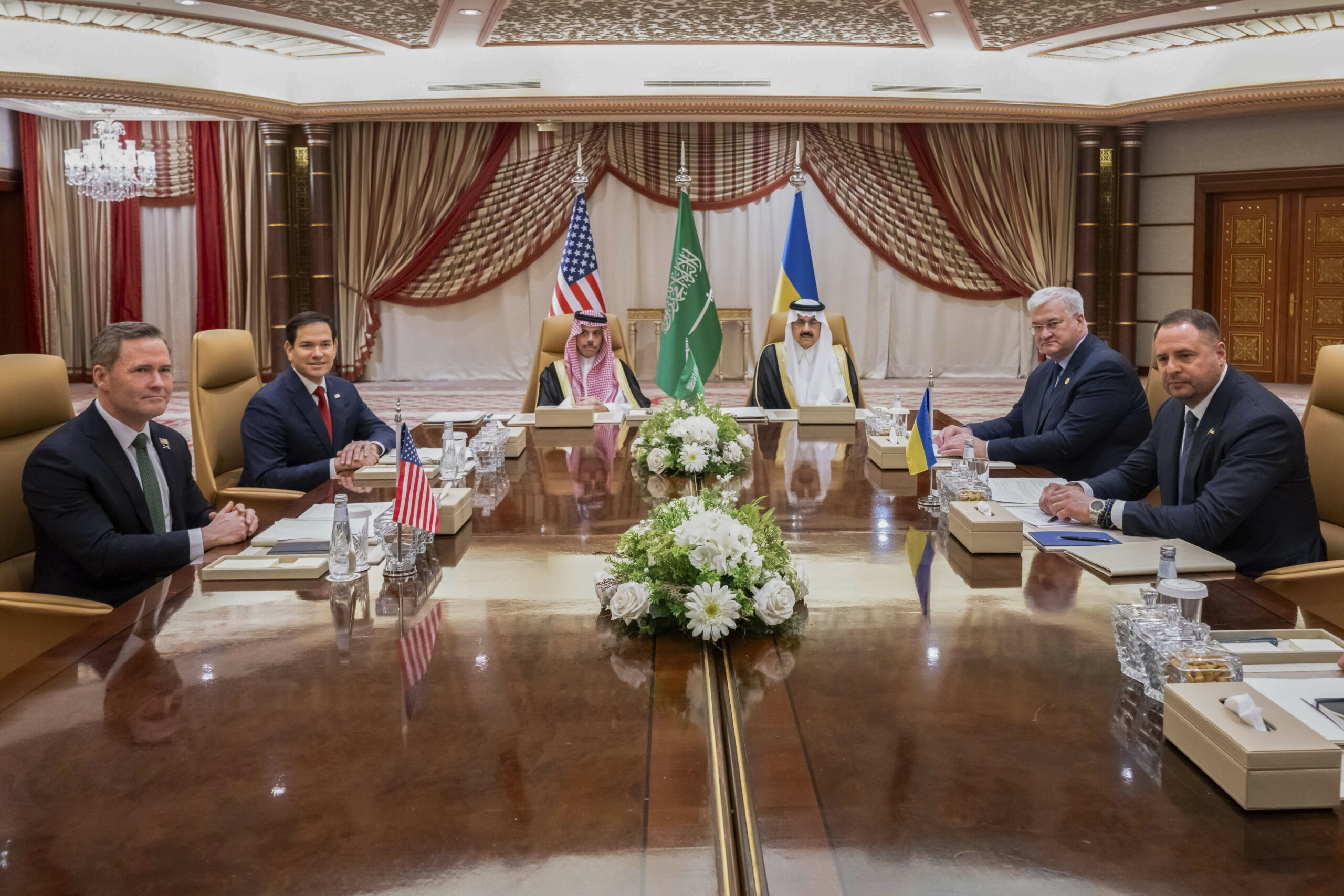 Mike Waltz (l-r), nationaler Sicherheitsberater der USA und US-Außenminister Marco Rubio sitzen dem ukrainische Außenminister Andrii Sybiha und dem ukrainische Leiter des Präsidialamtes, Andriy Yermak gegenüber. Zwischen beiden Parteien sitzen der saudi-arabische Außenminister Prinz Faisal bin Farhan und der nationale Sicherheitsberater Mosaad bin Mohammad al-Aiban. Im Hintergrund sind die Flaggen der USA, der Ukraine und Saudi-Arabiens zu sehen.