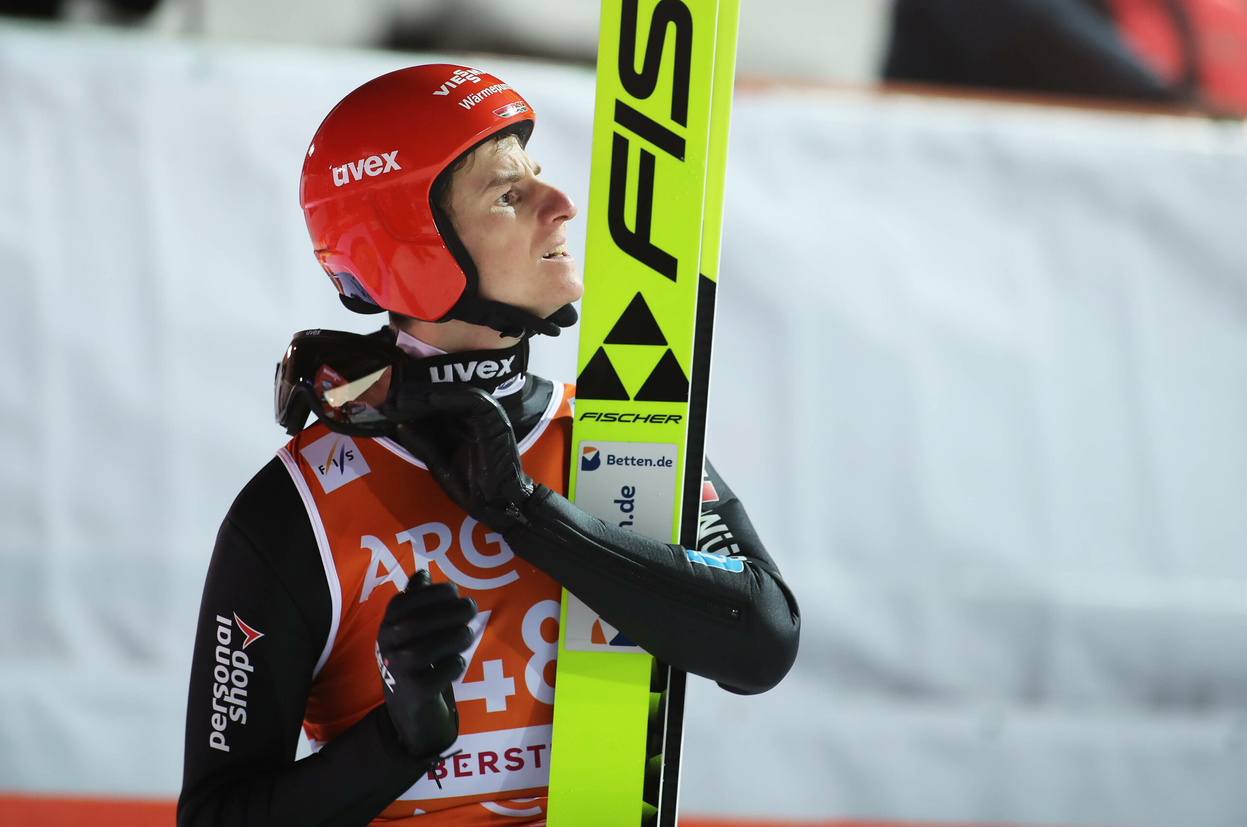 Karl Geiger öffnet seinen Helm mit Skiern in der Hand