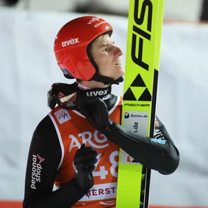 Karl Geiger öffnet seinen Helm mit Skiern in der Hand