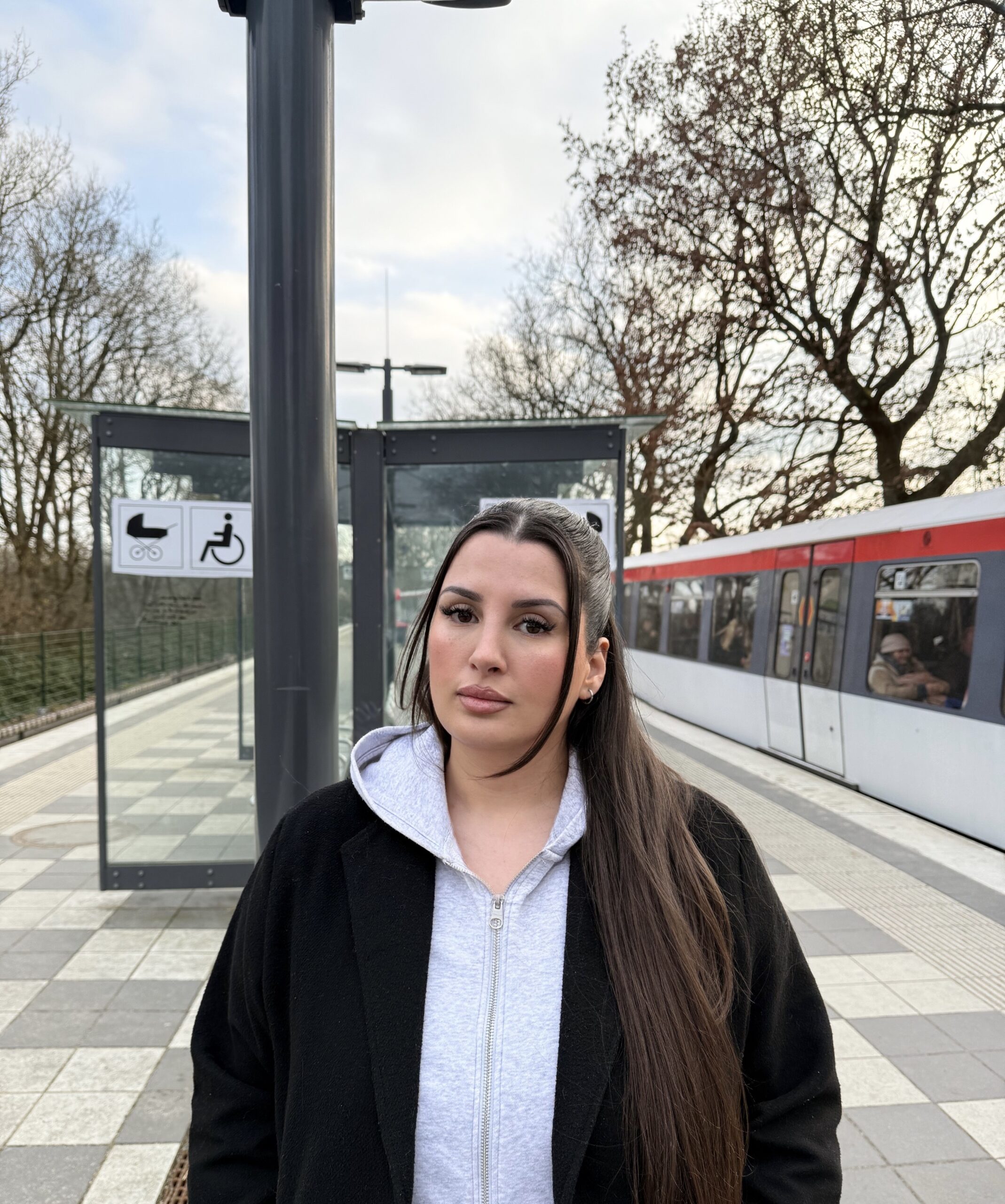 Junge Frau mit langen dunklen Haaren auf einem Bahnsteig