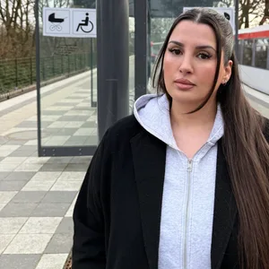 Junge Frau mit langen dunklen Haaren auf einem Bahnsteig