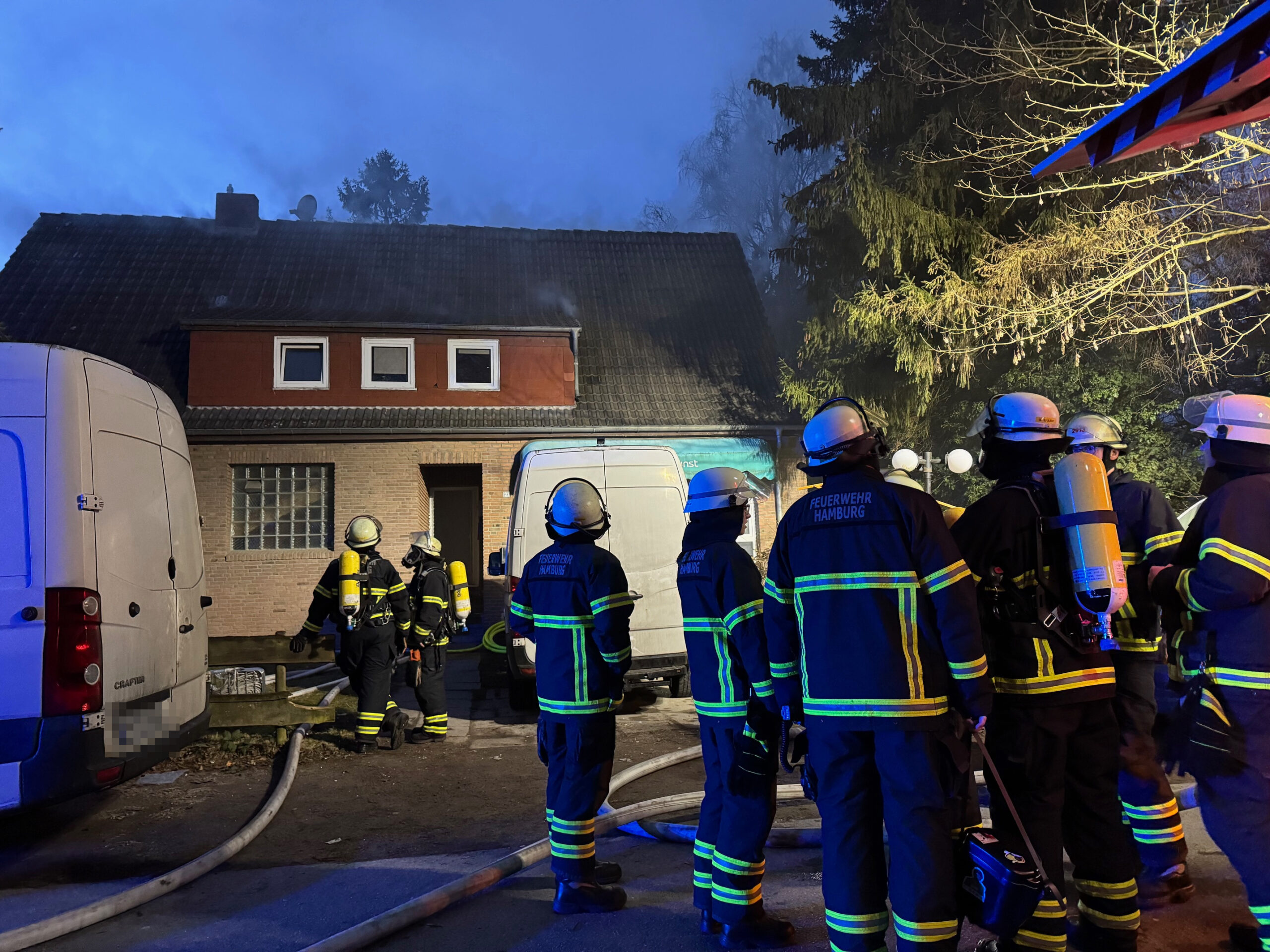 Feuerwehrkräfte stehen vor dem brennenden Haus.