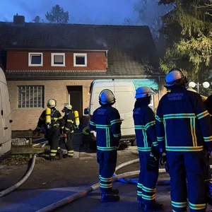 Feuerwehrkräfte stehen vor dem brennenden Haus.