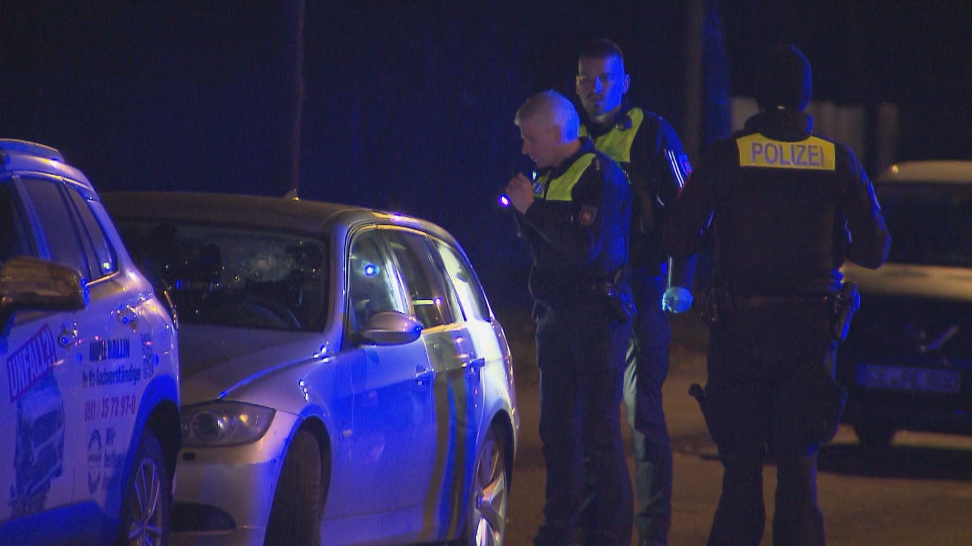 Polizisten mit einer Taschenlampe neben einem Wagen mit Loch in der Windschutzscheibe
