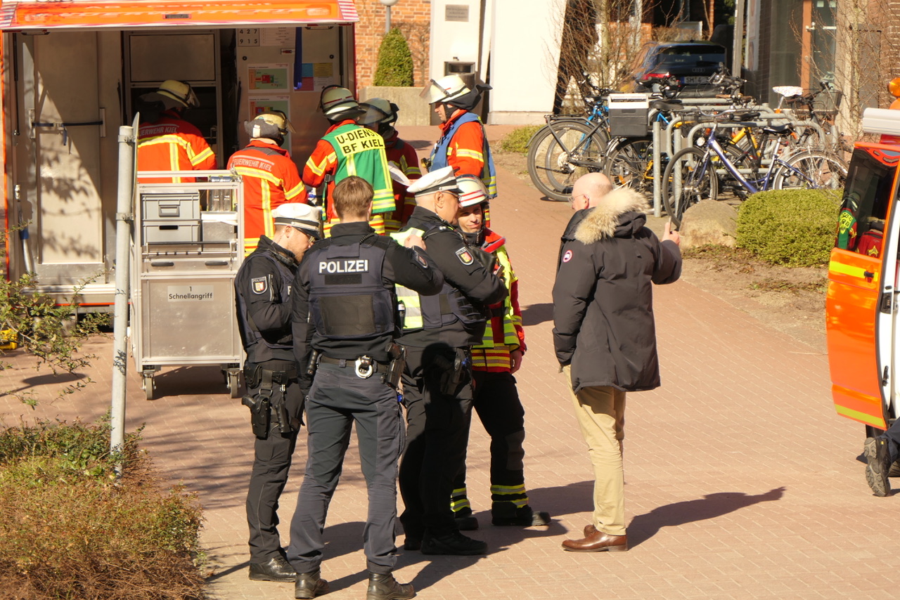 Mitarbeiter von Polizei und Feuerwehr stehen vor dem Verwaltungsgebäude der Uniklinik.