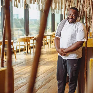 Chefkoch und Inhaber Louis-Lord Larbi vom Akan Afrofusion steht in seinem Restaurant. Im Hintergrund sieht man Tische und Stühle.