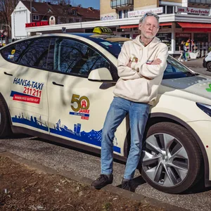 Manfred Bley (Taxifahrer) steht vor seinem Taxi-Wagen von der Marke „Tesla“
