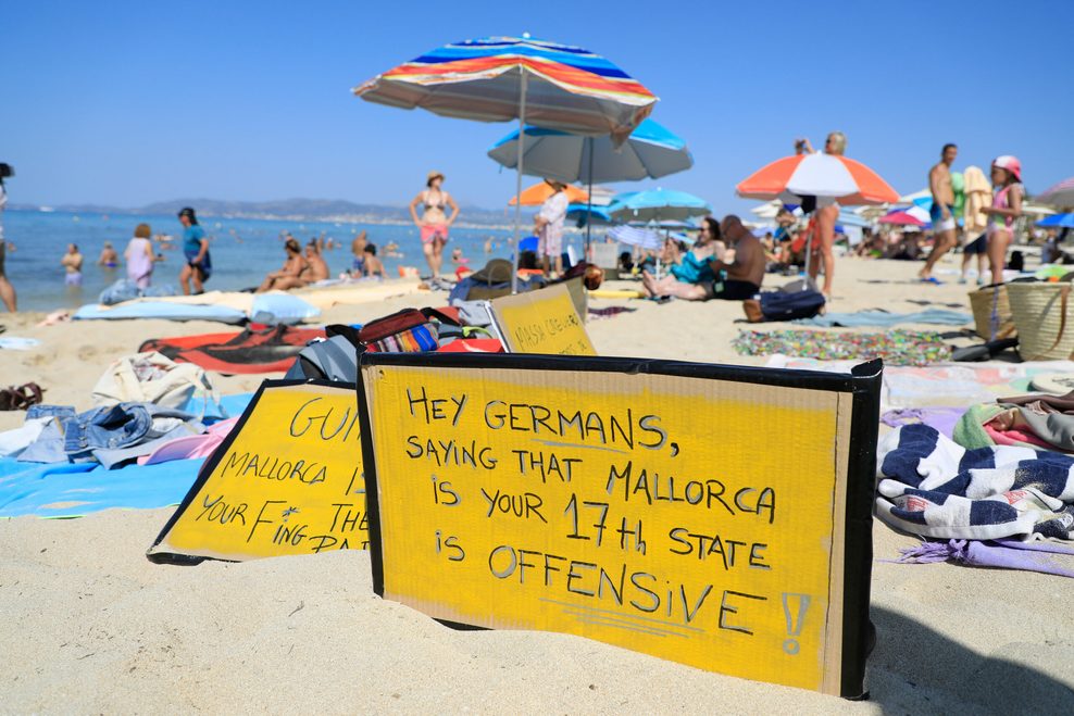 „Hallo Deutsche, zu sagen, dass Mallorca euer 17. Bundesland ist, ist offensiv-aggressiv" steht auf einem Schild an einem Strand auf Mallorca.