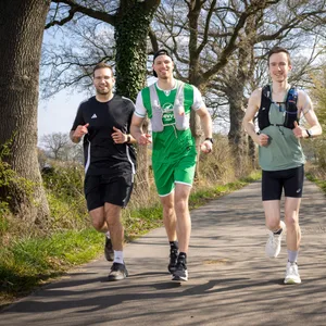 Drei Männer joggen auf einem Weg im Grünen.