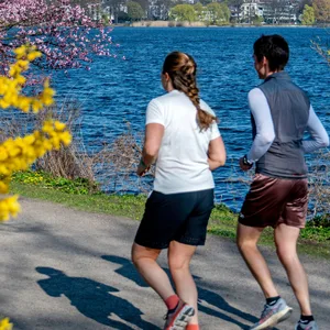 Zwei Frauen joggen bei frühlingshaftem Wetter auf einem Weg an der Außenalster.