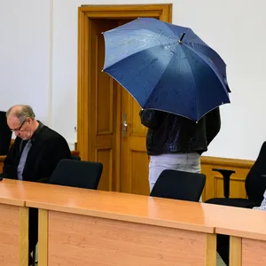 Ein Angeklagter versteckt sich unter einem blauen Regenschirm