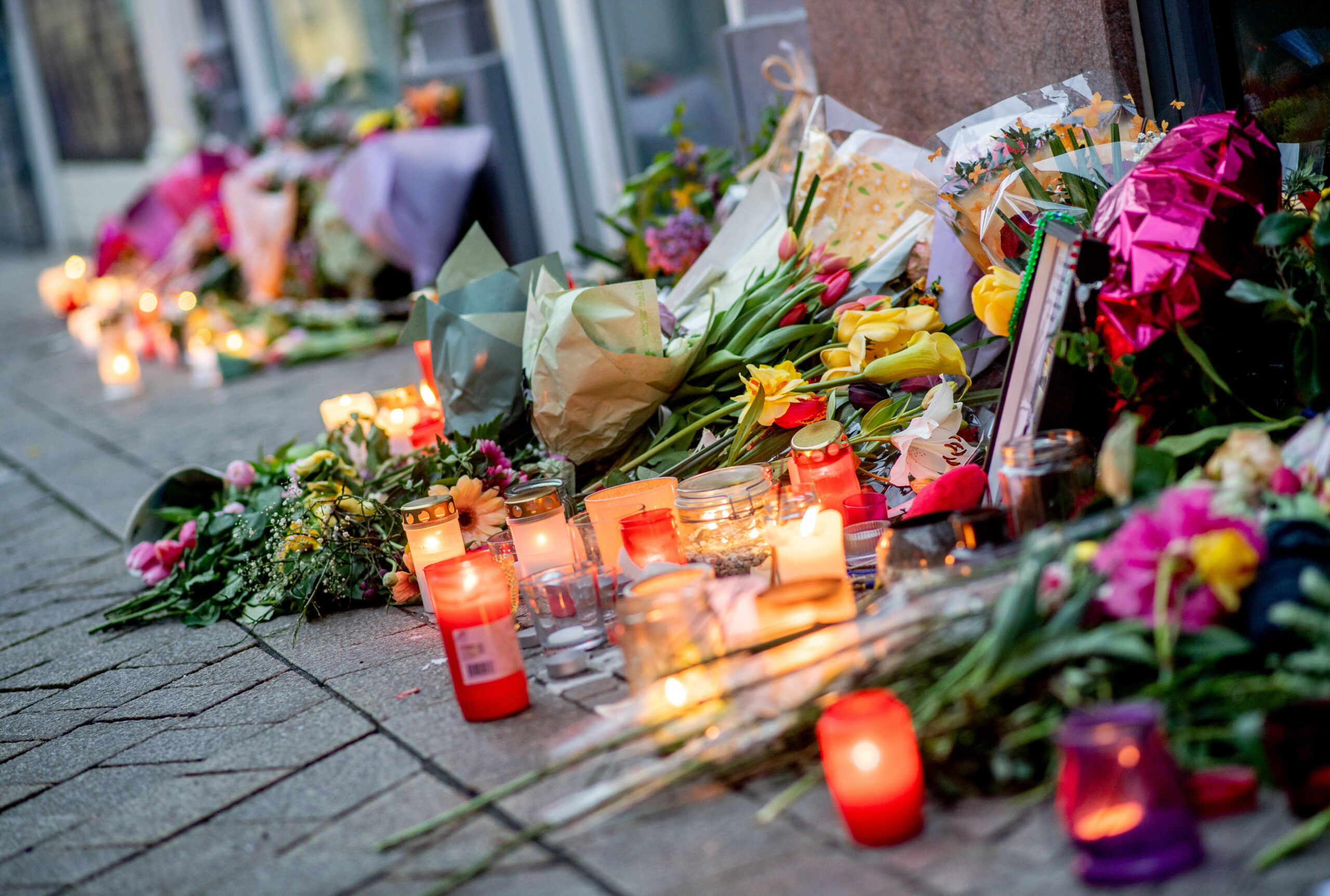 Zahlreiche Blumen und Kerzen stehen in der Innenstadt an einer Hauswand.