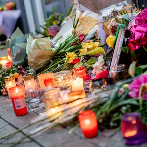 Zahlreiche Blumen und Kerzen stehen in der Innenstadt an einer Hauswand.
