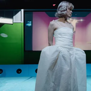 Eine Schauspielerin steht in weißem langen Kleid auf der Bühne.