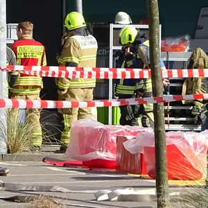 Mehrere Einsatzkräfte stehen hinter Absperrband, vor der Rewe-Filiale