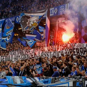 Auf der Nordtribüne brennt Pyrotechnik, die HSV-Fans kritisieren mit einem Banner die Ticket-Preise