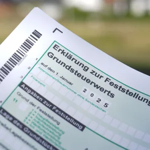 Ein Erklärung zur Feststellung des Grundsteuerwerts für das Jahr 2025 wird vor eine Wohnsiedlung hochgehalten.