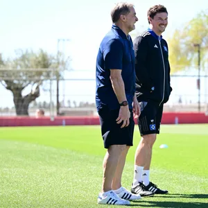 Stefan Kuntz und Merlin Polzin lachen bei ihrem Gespräch auf dem Trainingsplatz