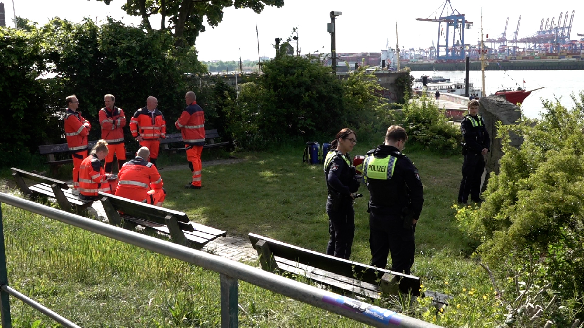 Rettungskräfte und Polizisten stehen in Övelgönne auf einer Wiese.