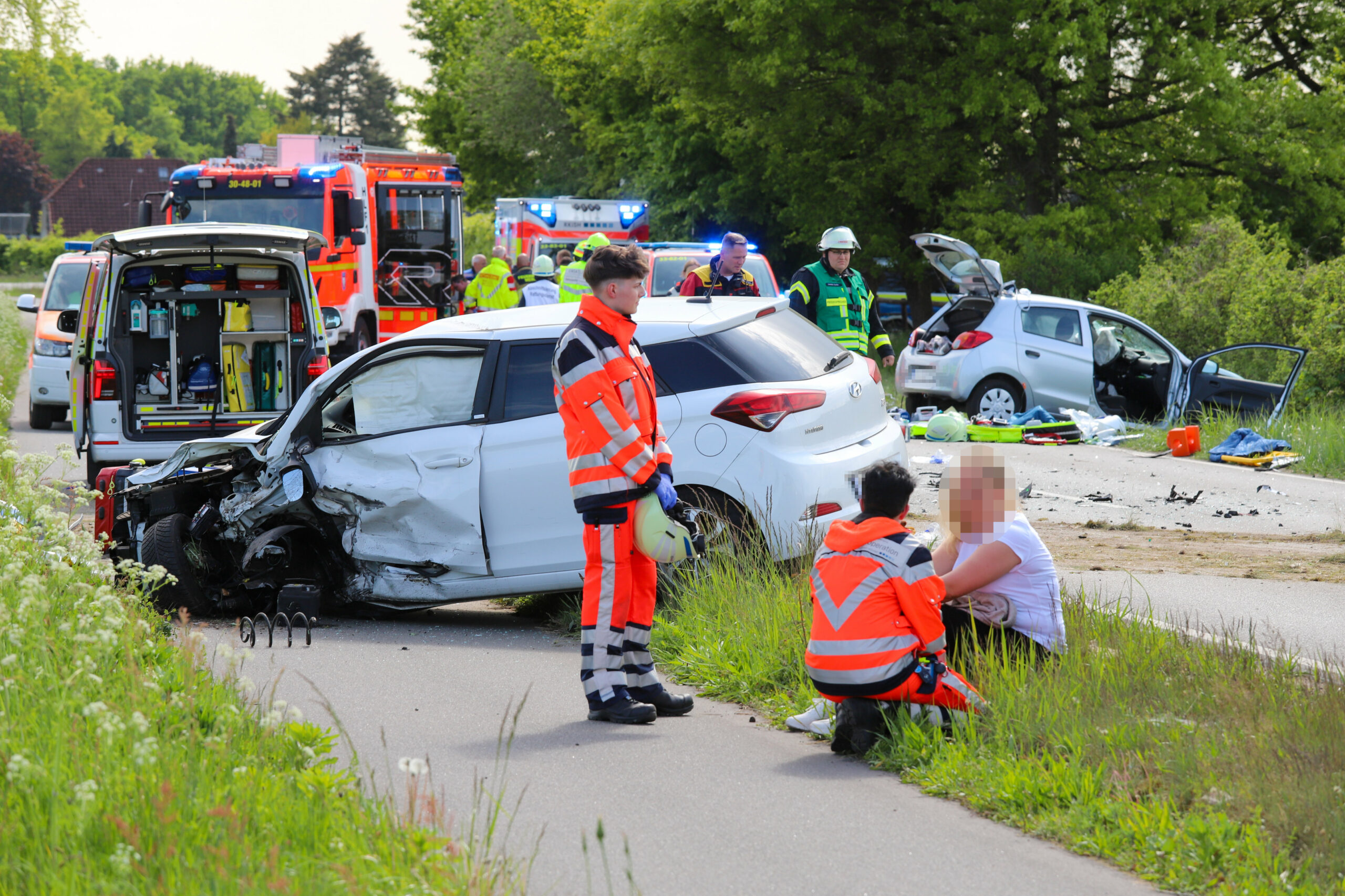 Rettungskräfte stehen am Unfallort mit zwei verunfallten Autos.