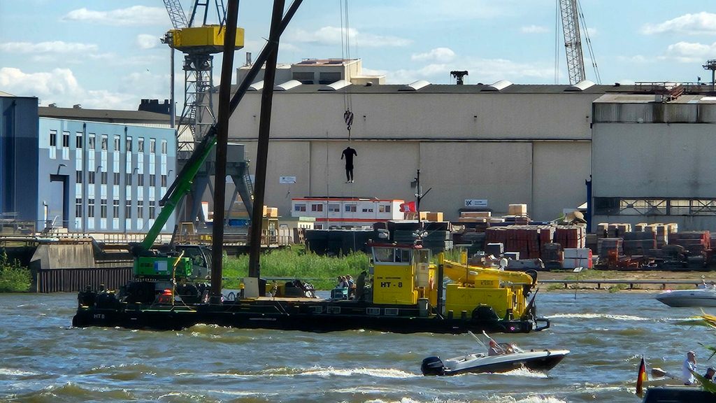 An einem Ponton auf der Elbe baumelt eine kopflose Puppe am Kran.