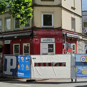 Bauzaum vor einem rot-gelben Eckhaus