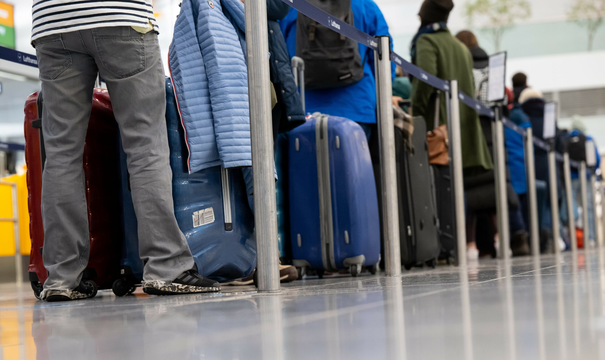 Passagiere stehen mit ihrem Gepäck an Check-in-Schaltern am Flughafen.