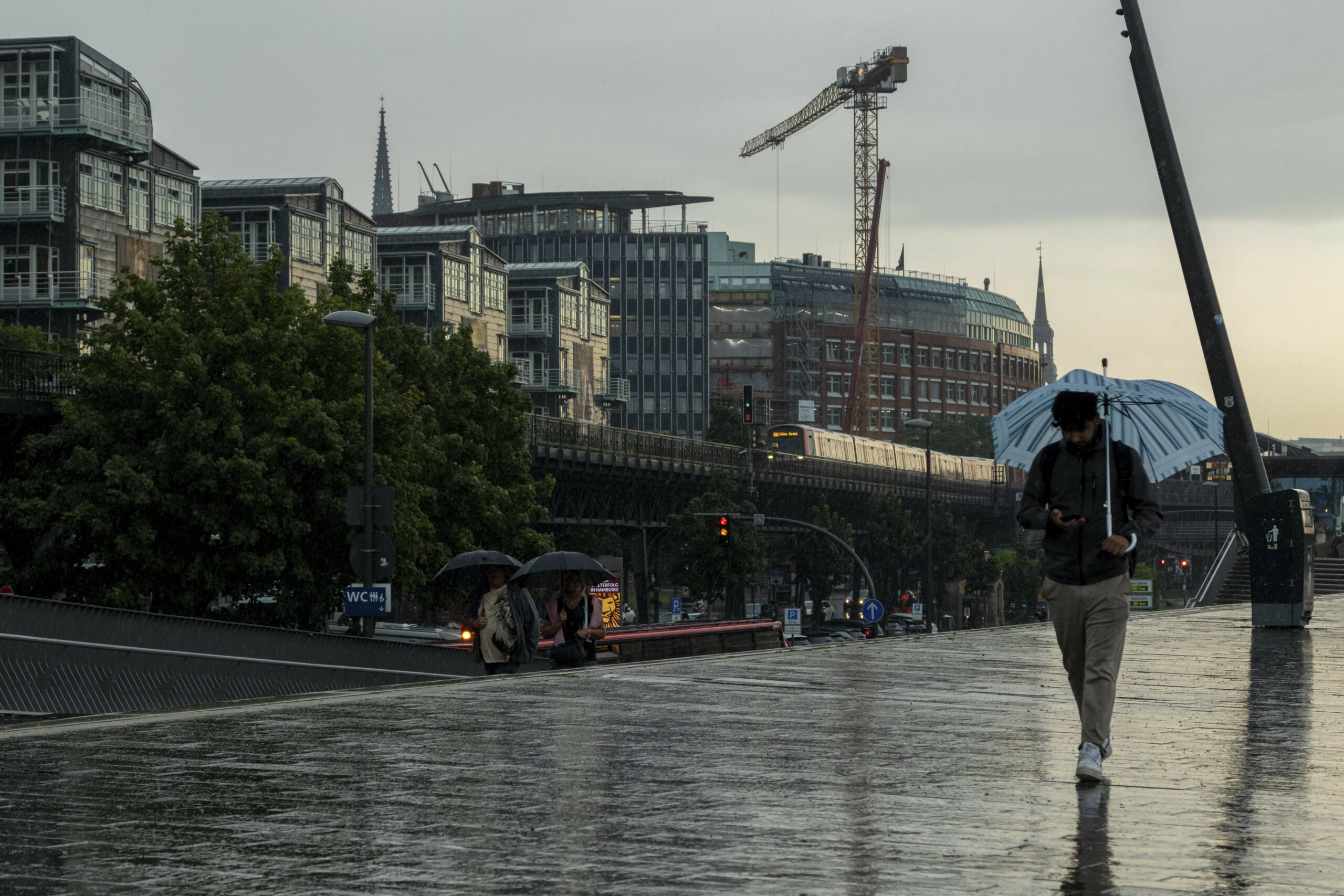 Tourist mit Regenschirm unterwegs im Regen neben der U-Bahn Linie U3 an den Landungsbrücken im Hafen von Hamburg