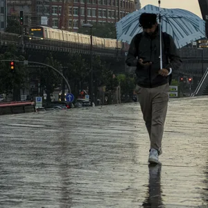 Tourist mit Regenschirm unterwegs im Regen neben der U-Bahn Linie U3 an den Landungsbrücken im Hafen von Hamburg