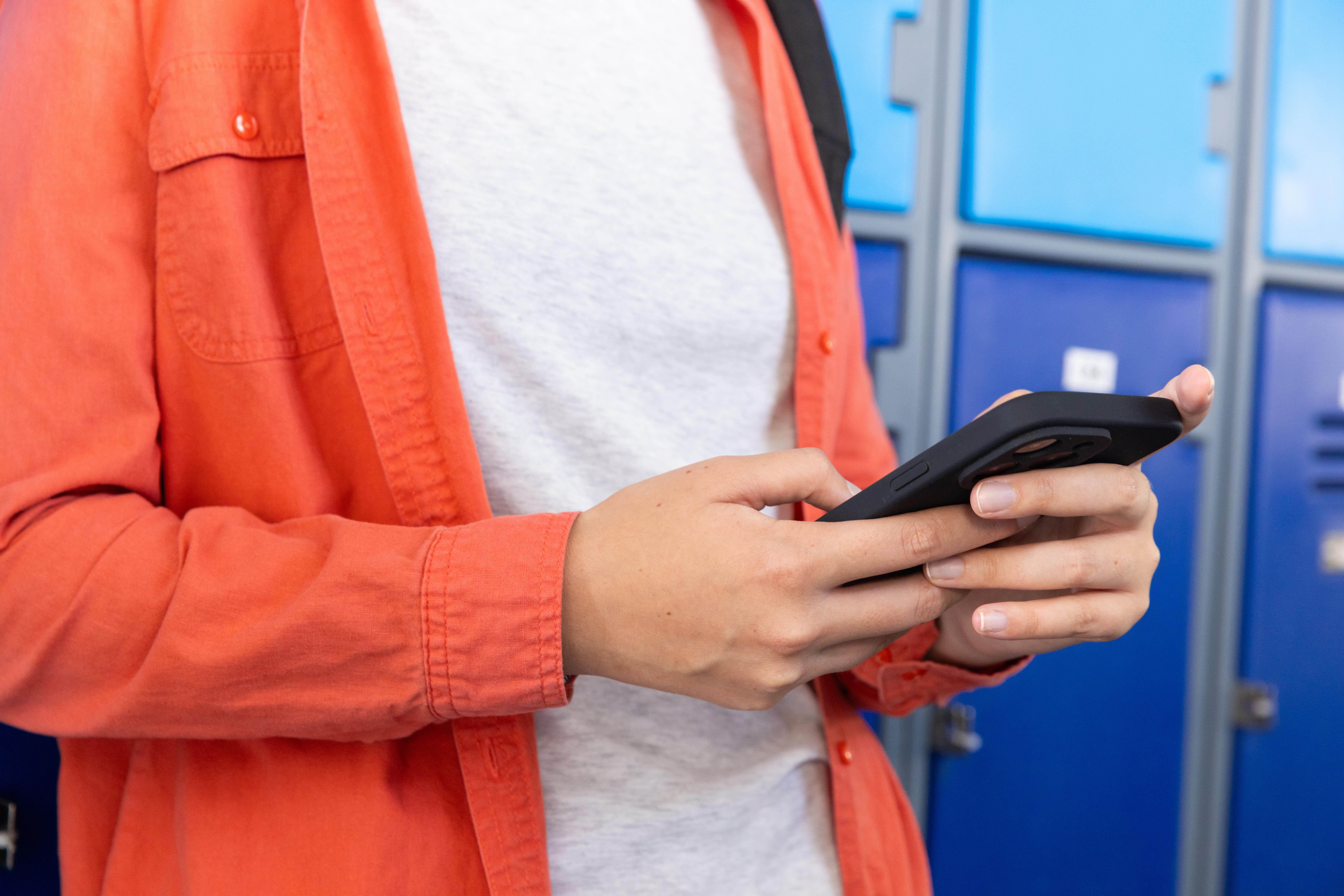 Eine Person steht vor Schulspinden und hält ein Handy in der Hand
