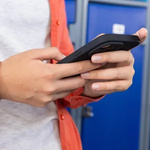 Eine Person steht vor Schulspinden und hält ein Handy in der Hand