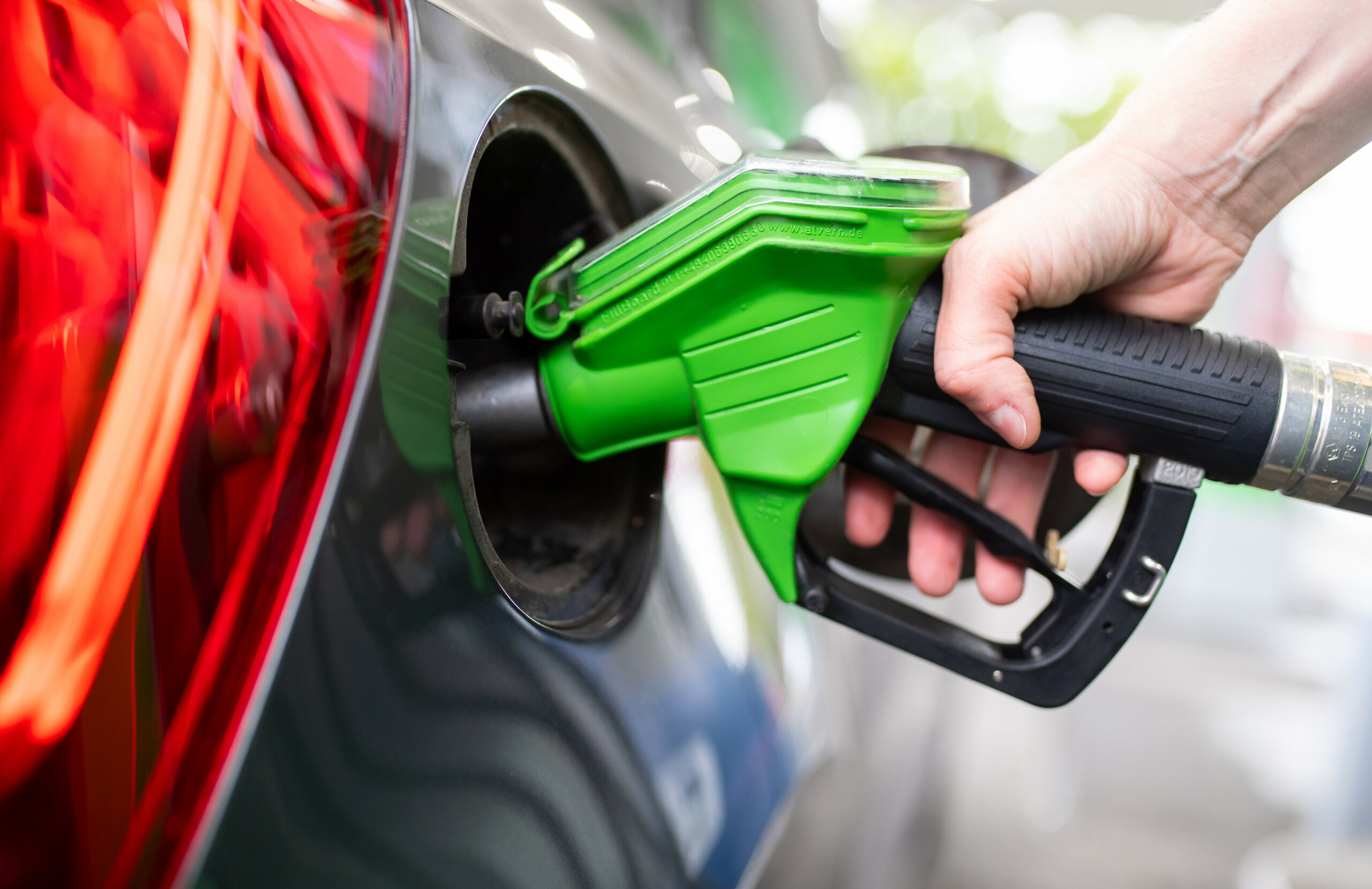 Eine Frau hält an einer Tankstelle an einer Zapfsäule eine Zapfpistole in der Hand und betankt ein Auto.