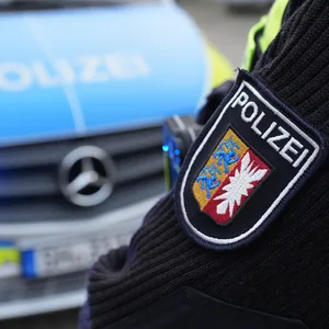 Das Landeswappen von Schleswig-Holstein und der Schriftzug „Polizei“ sind auf dem Ärmel einer Polizistin vor einem Einsatzfahrzeug zu sehen.