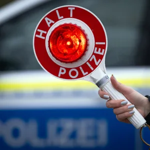 Eine Polizistin hält während einer Verkehrskontrolle eine Polizeikelle mit der Aufschrift „Halt Polizei“. (Symbolbild)