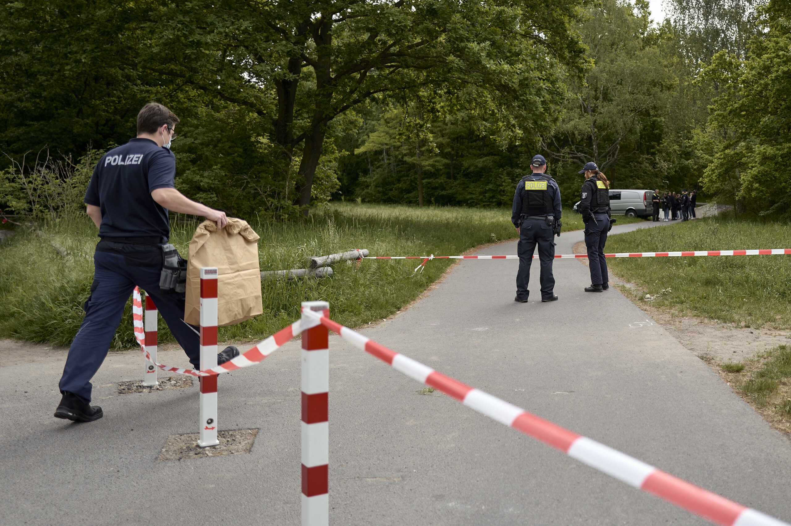 Einsatzkräfte der Polizei stehen hinter einer Absperrung an einem Weg im Stadtteil Gropiusstadt im Bezirk Neukölln