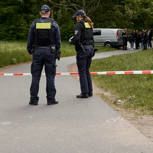 Einsatzkräfte der Polizei stehen hinter einer Absperrung an einem Weg im Stadtteil Gropiusstadt im Bezirk Neukölln
