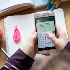 Eine Schülerin sitzt mit ihrem Handy und ihren Schulsachen an einem Schreibtisch.