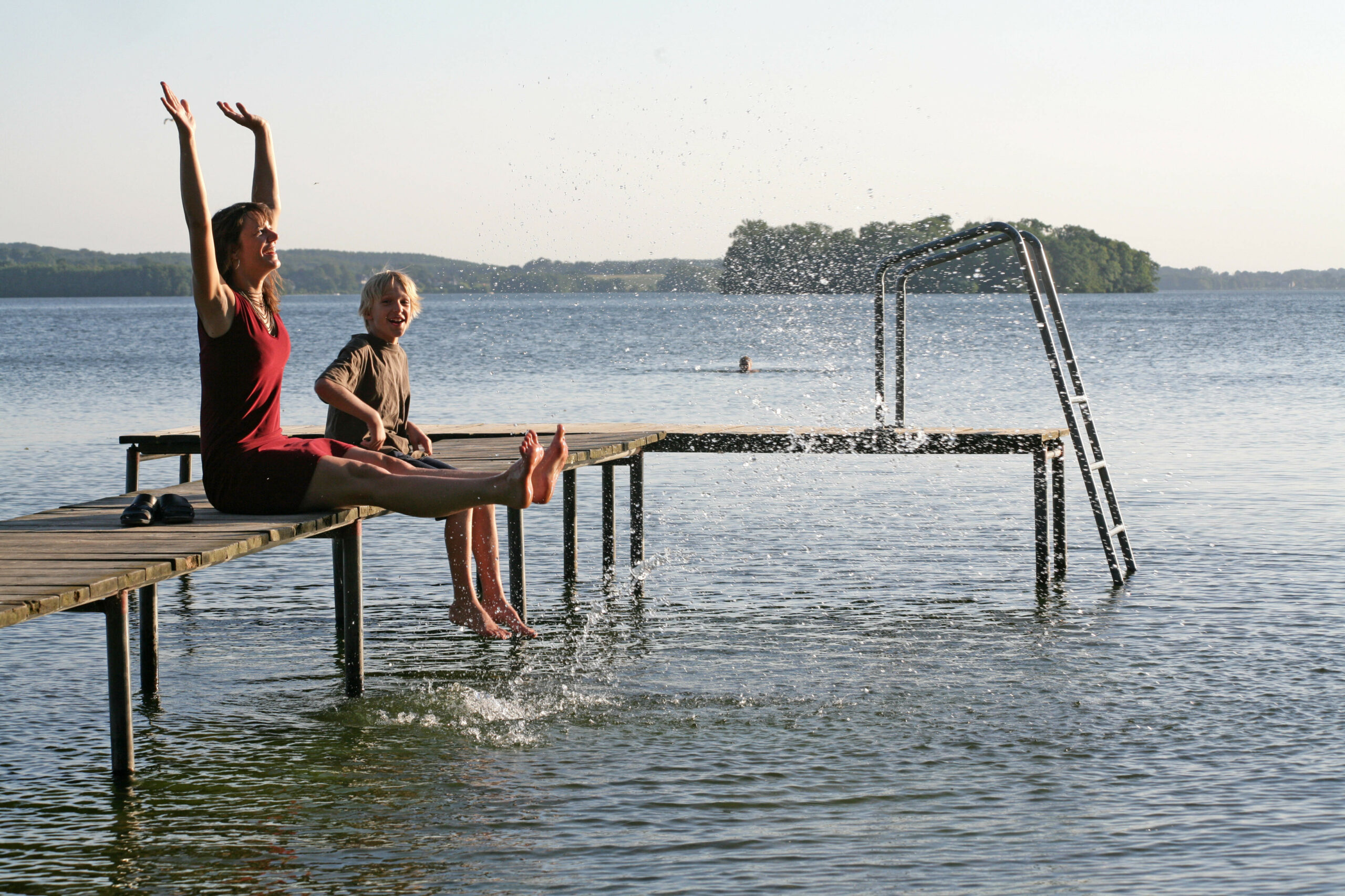 Eine Frau und ein Kind sitzen auf einem Steg am Großen Plöner See.