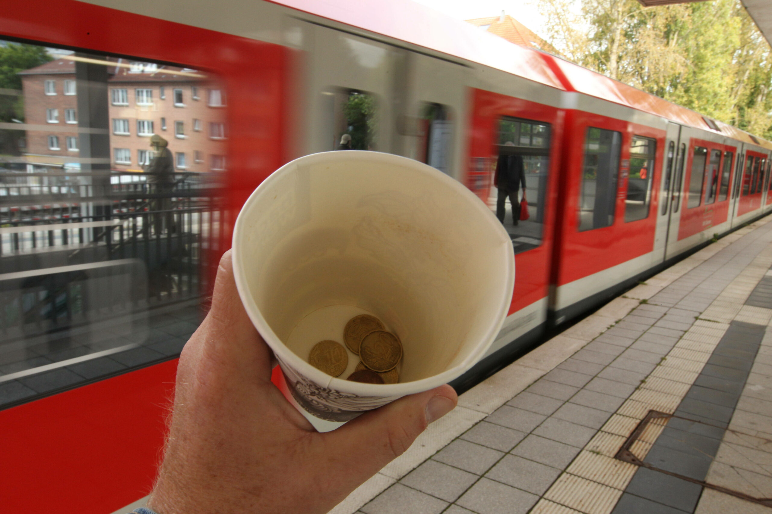 ein Pappbecher mit Geld vor einem Zug (Symbolbild)