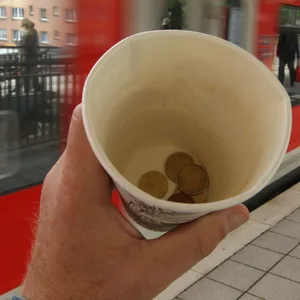 ein Pappbecher mit Geld vor einem Zug (Symbolbild)