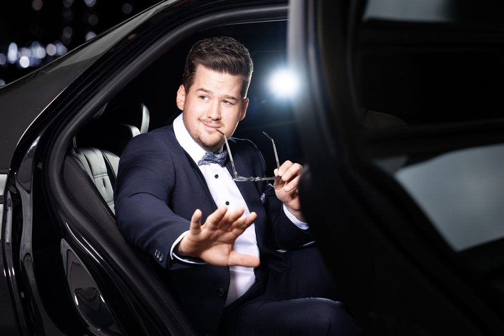 Er sitzt in Anzug mit Fliege in einer Limousine