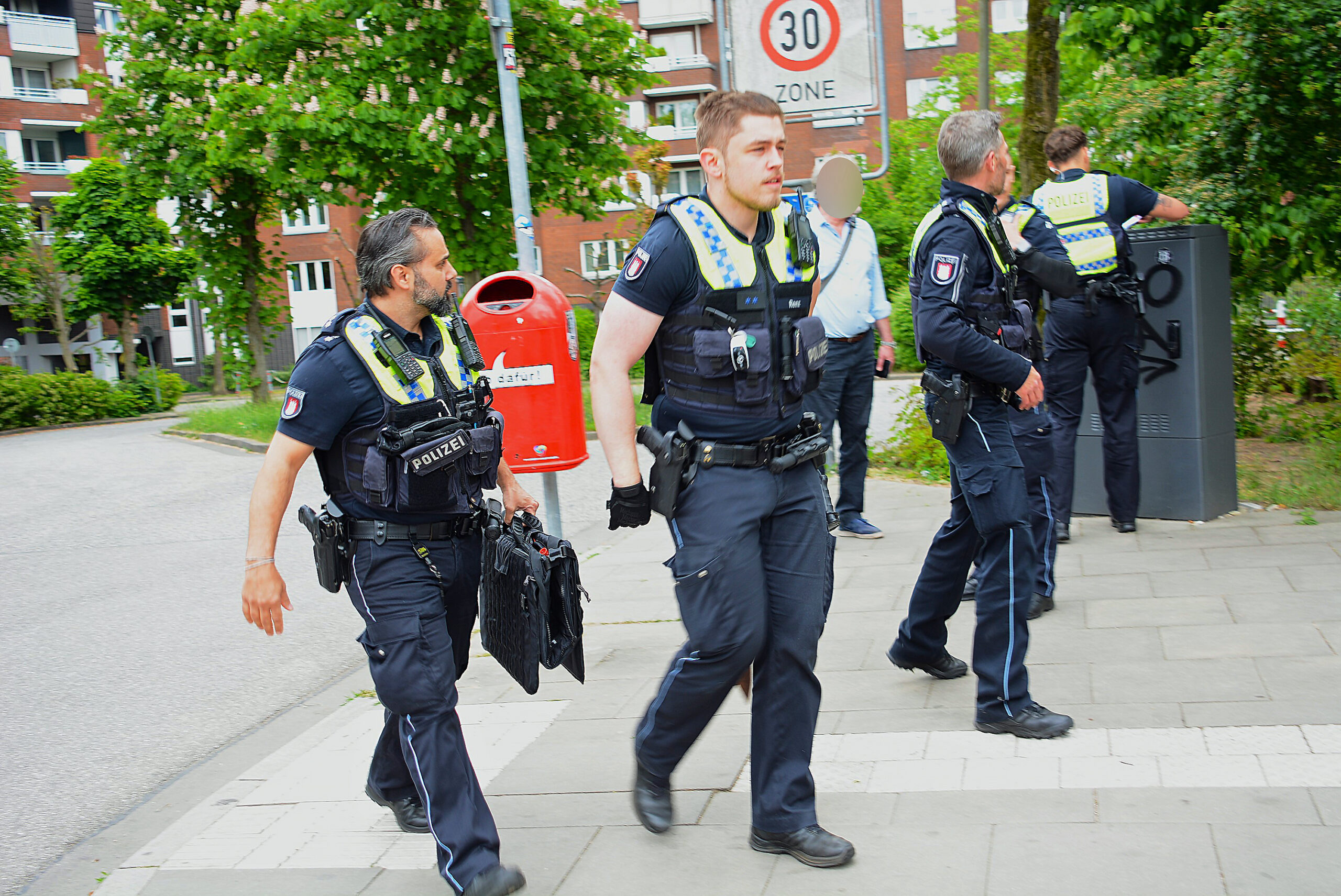 Polizisten in Lohbrügge im Einsatz. Ein Beamter (M.) versteckt die sichergestellte Waffe hinter seinem Rücken.