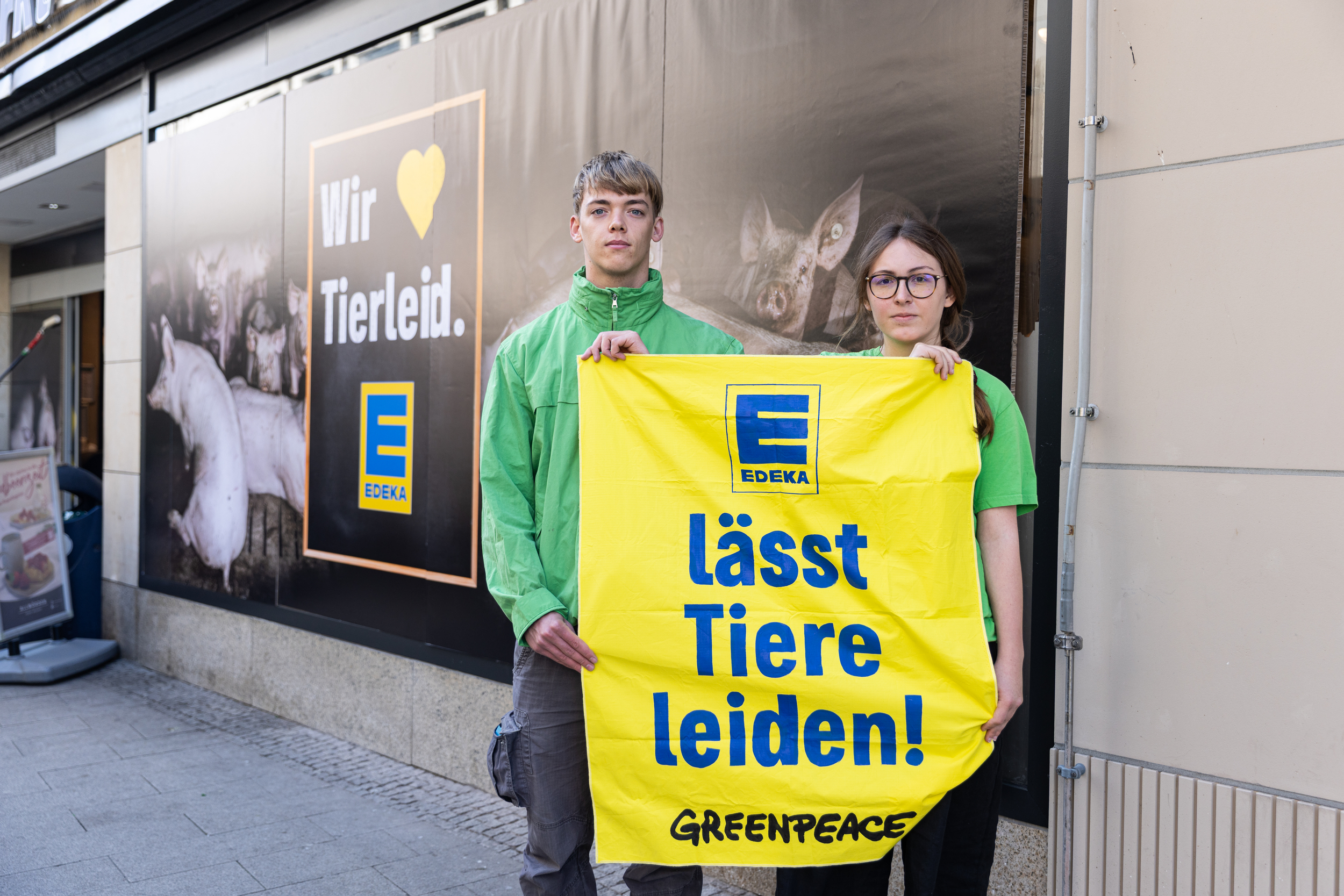 Zwei Aktivist:innen halten am „Edeka Schlemmer Markt Struve“ ein Plakat mit der Aufschrift „Edeka lässt Tiere leiden“ in die Höhe.