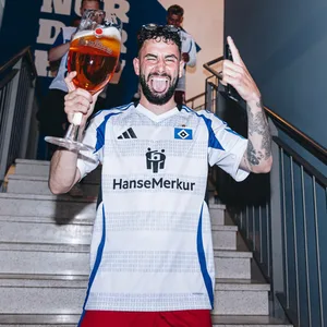 Marco Richter lächelt mit Bierglas in der Hand im Treppenhaus des HSV-Stadions