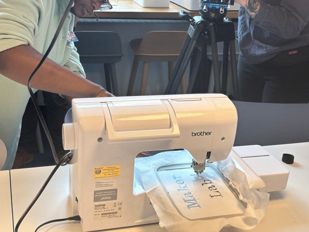 Eine Stickmaschine stickt die Aufschrift „MakerLab“ auf ein Stück Stoff.