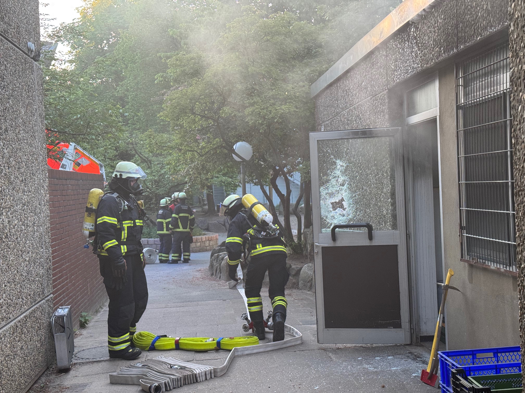 Die Feuerwehr löscht den Brand an der Rudolf-Steiner-Schule in Farmsen. An der Glastür sind Einbruchspuren zu erkennen.