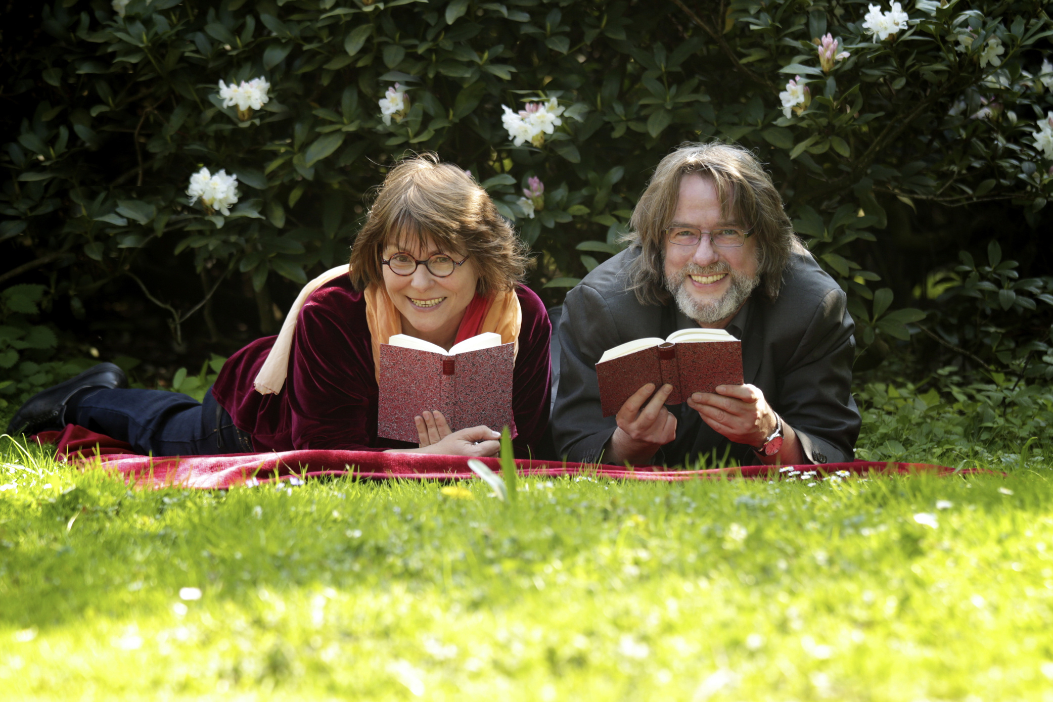 Vera Rosenbusch und Lutz Flörke liegen mit Büchern in der Hand auf einer Wiese.