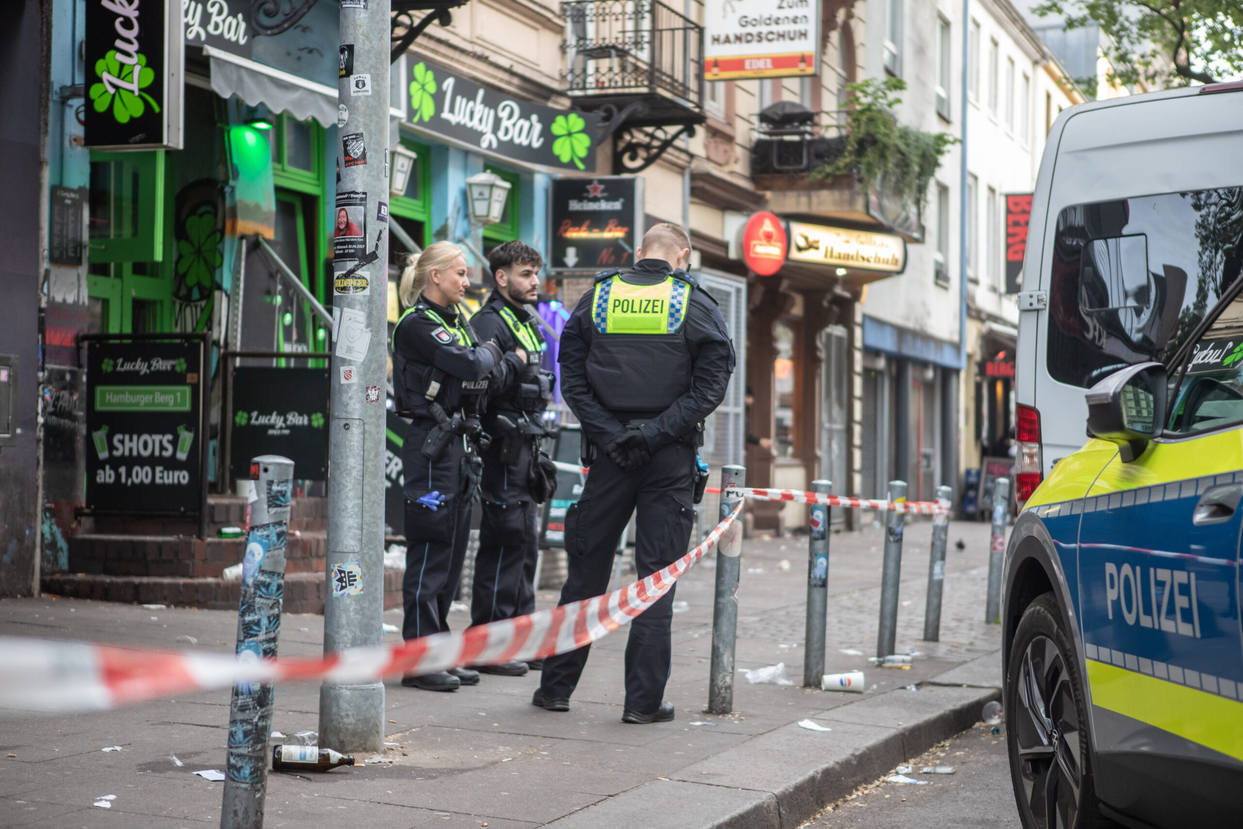 Polizisten stehen in einem abgesperrten Bereich vor einer bar.