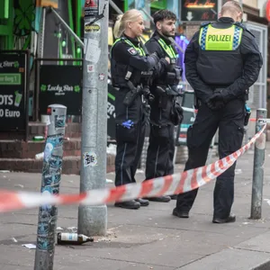 Polizisten stehen in einem abgesperrten Bereich vor einer bar.