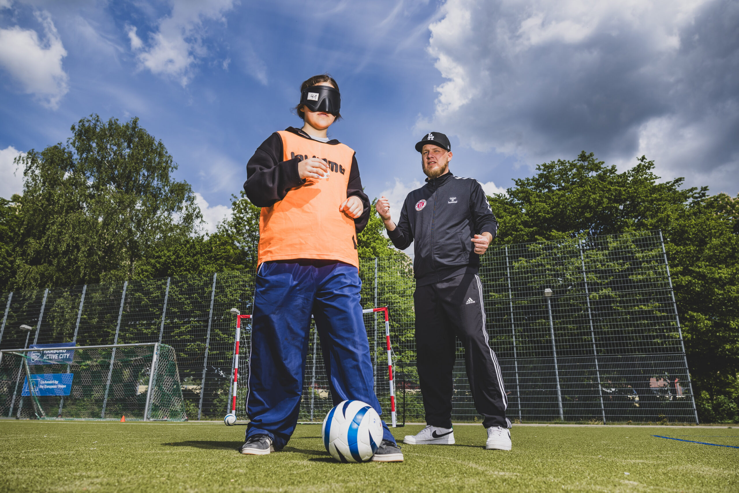 St. Paulis Blindenfußballer Viktor Faul erklärt Schülerin Vida, wie sich der Ball auch verdunkelt spielen lässt.